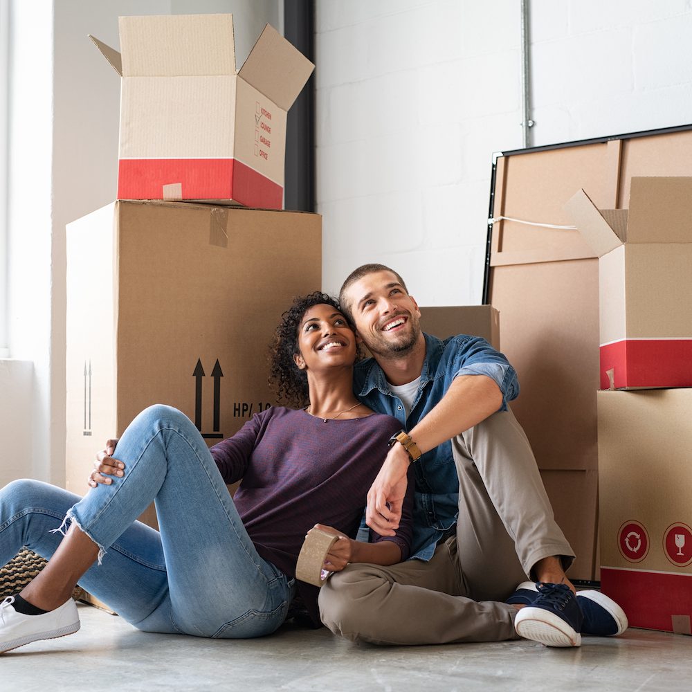 Young couple resting after moving into a new home and daydreaming. Multiethnic contemplative couple sitting on floor and thinking about their future while looking up. Happy married couple buy new apartment and plan a family.