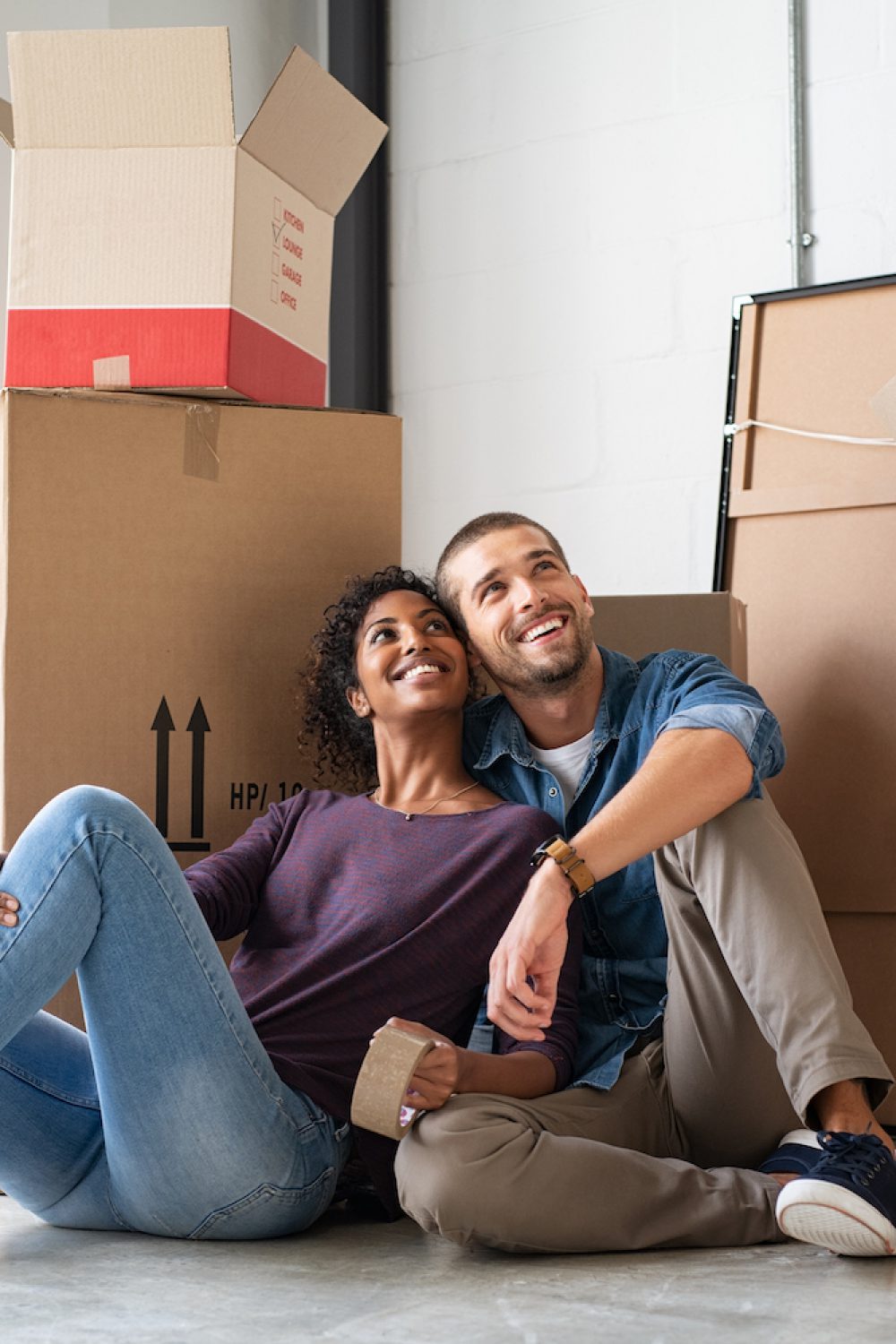 Multiethnic couple in new home with boxes Young couple resting after moving into a new home and daydreaming. Multiethnic contemplative couple sitting on floor and thinking about their future while looking up. Happy married couple buy new apartment and plan a family.